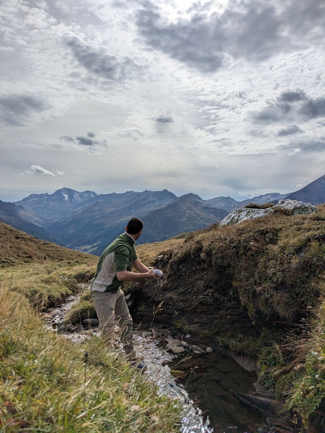 Expedition traveler gathering water from a clear mountain stream in scenic high-altitude terrain